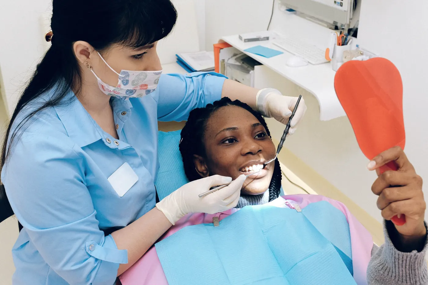 A dentist examining a patient's teeth, with the patient holding a hand mirror
