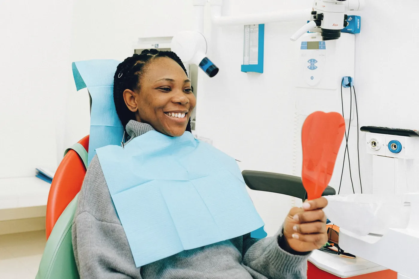 A smiling patient in a dental chair holding a hand mirror